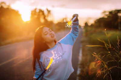 Woman with arms raised on field against sky during sunset