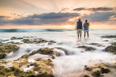 Rear view of couple on beach against sky during sunset