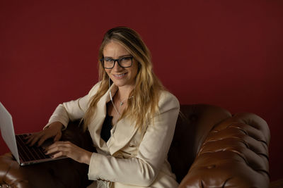 Woman working at home with laptop classic brown arm chair. red  wall home office. gray notebook 