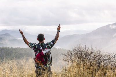 Rear view of traveler with his dog on the mountain raising arms