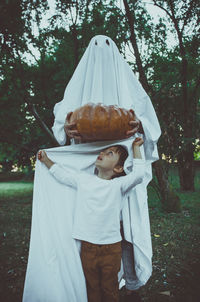 Cute boy with person wearing ghost costume in park at sunset during halloween
