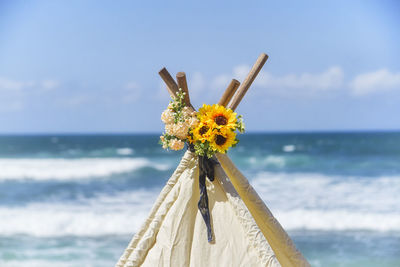 Close-up of yellow flower on beach against sky. bouquet of flowers decoration on top of teepee tent