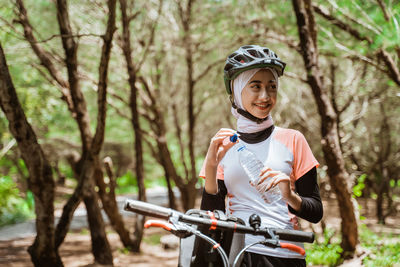 Smiling woman holding water bottle against tree