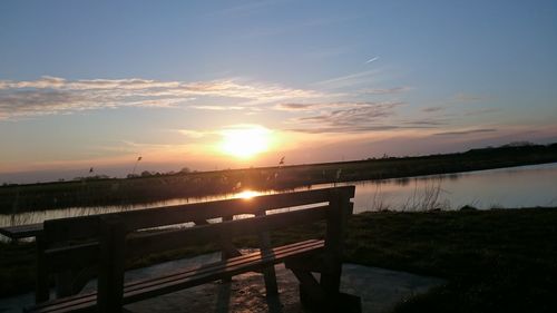 Close-up of railing by lake against sky during sunset