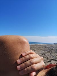 Close-up of man lying down at beach against blue sky