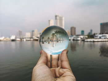 Close-up of hand holding crystal ball against river