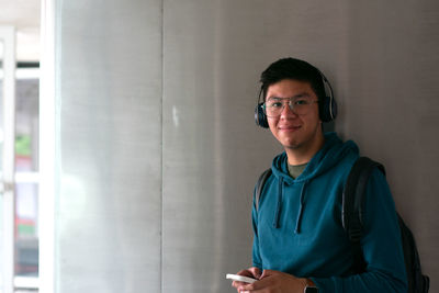 A young man watching the camera smiling and holding his smartphone