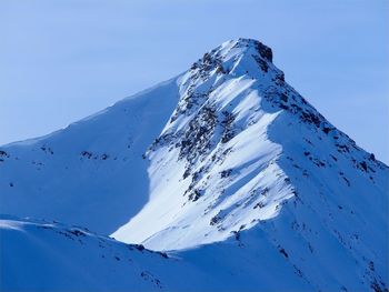 Low angle view of snowcapped mountains against clear blue sky