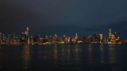 Illuminated buildings by sea against sky at night