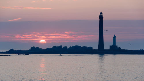 Silhouette lighthouse by sea against sky during sunset