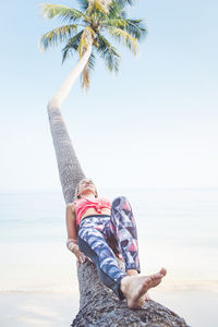 Woman lying on coconut palm tree at beach during summer