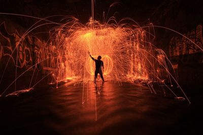 Silhouette man performing wire wool at pond