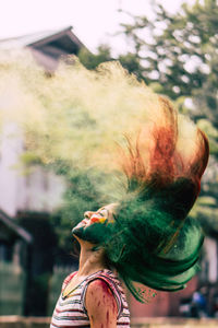 Woman splashing powder paint with hair against tree