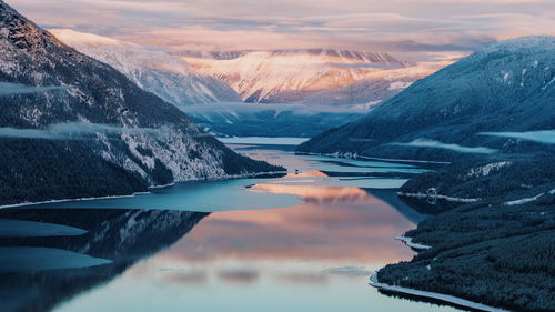 Scenic view of lake and mountains against cloudy sky during winter