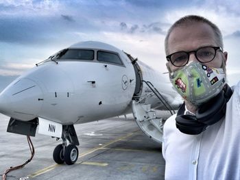 Portrait of man standing by airplane against sky