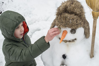 Cute boy making snowman in yard during winter
