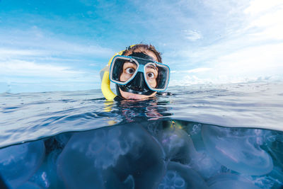 A woman in a black wetsuit is in the water with jellyfish. the jellyfish are floating around her