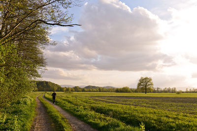 Person jogging on field against cloudy sky