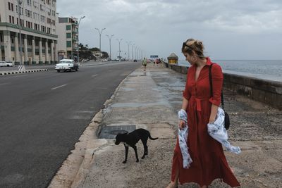 Full length of woman standing on road against cloudy sky in city