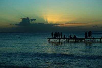 Silhouette people on pier over sea against sky during sunset