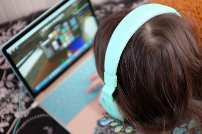 High angle view of woman listening through headphones while using laptop at home