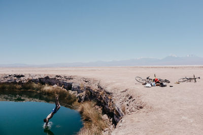 Shirtless man jumping in lake at desert