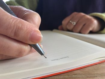 Cropped hand of woman writing in book at home