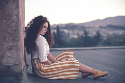 Young woman with curly hair looking away while sitting outdoors 