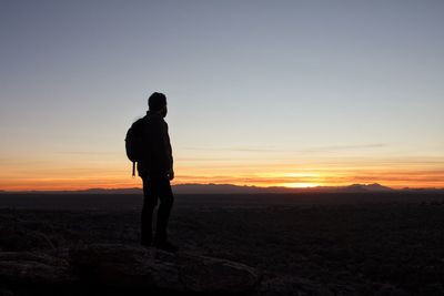 Silhouette man standing on field against sky during sunset