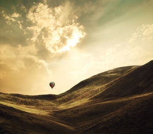 Hot air balloon flying over mountains against cloudy sky during sunset