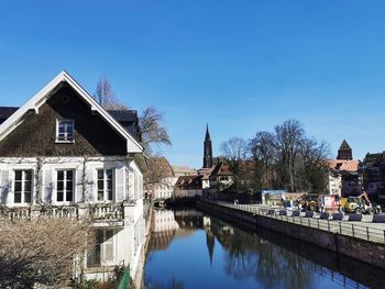 Buildings by river against clear blue sky