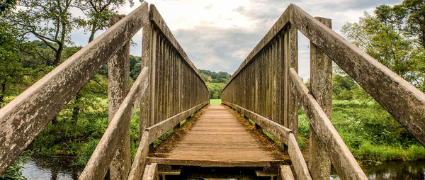 Wooden footbridge amidst trees against sky