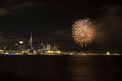 Firework display over illuminated city against sky at night