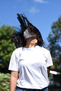 Young woman wearing mask standing against sky