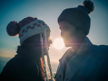 Close-up of couple in knit hats against sky during sunset