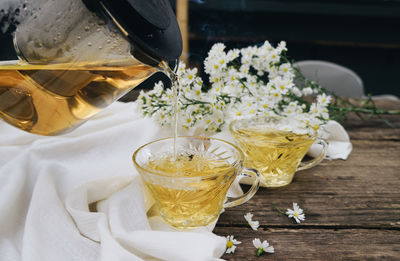 Close-up of drink in glass ,cups of tea with chamomile flowers and teapot on wooden background