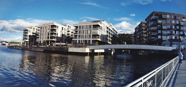 Bridge over river by buildings in city against sky