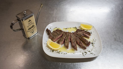 Grilled sliced beef steak with lemons and rosemary on a plate. oil bottle.