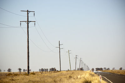 Electricity pylons on field against clear sky