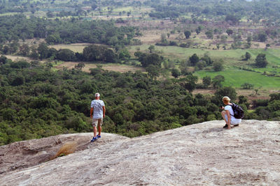 Rear view of man and woman standing on rock against trees