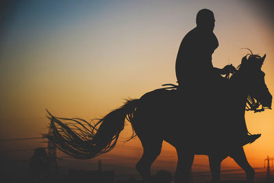 Silhouette man riding horse at sunset