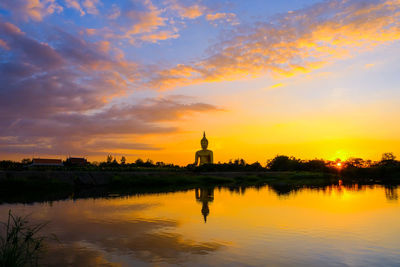 Reflection of silhouette buildings in lake against sky during sunset