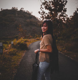 Young woman looking at camera while standing by trees