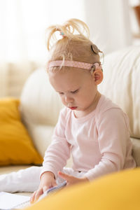 Portrait of cute baby girl sitting on bed at home