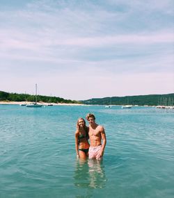 Portrait of smiling young couple standing in sea against sky