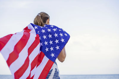 Rear view of woman holding flag against sky