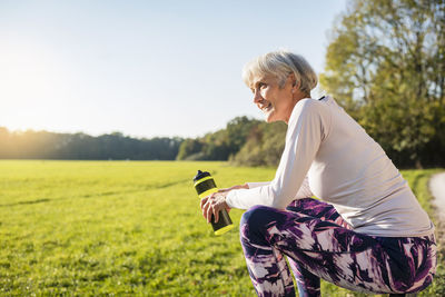 Smiling sportive senior woman holding bottle in rural landscape