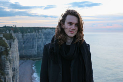 Happy man looking away while standing on cliff against sea during sunset