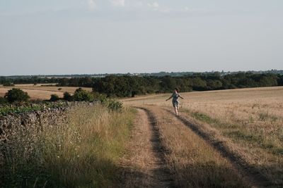 Rear view of man walking on field against sky