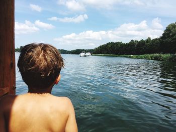 Rear view of shirtless boy looking at sea while standing against sky